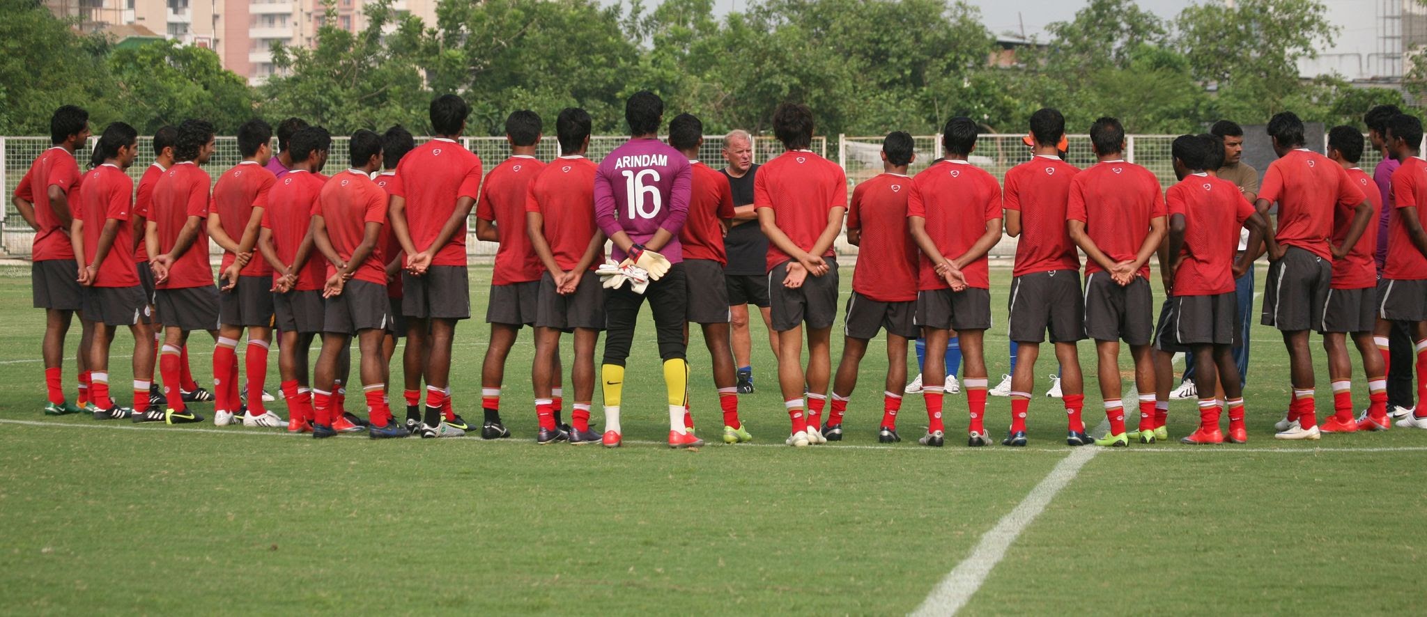 Youth football team training on pitch in red jerseys with coach