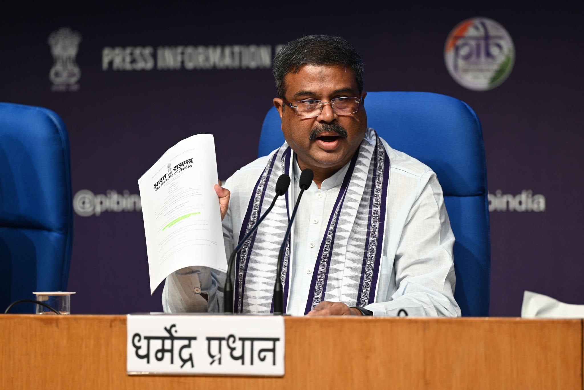 Union Education Minister Dharmendra Pradhan holding up an official gazette document at PIB press conference