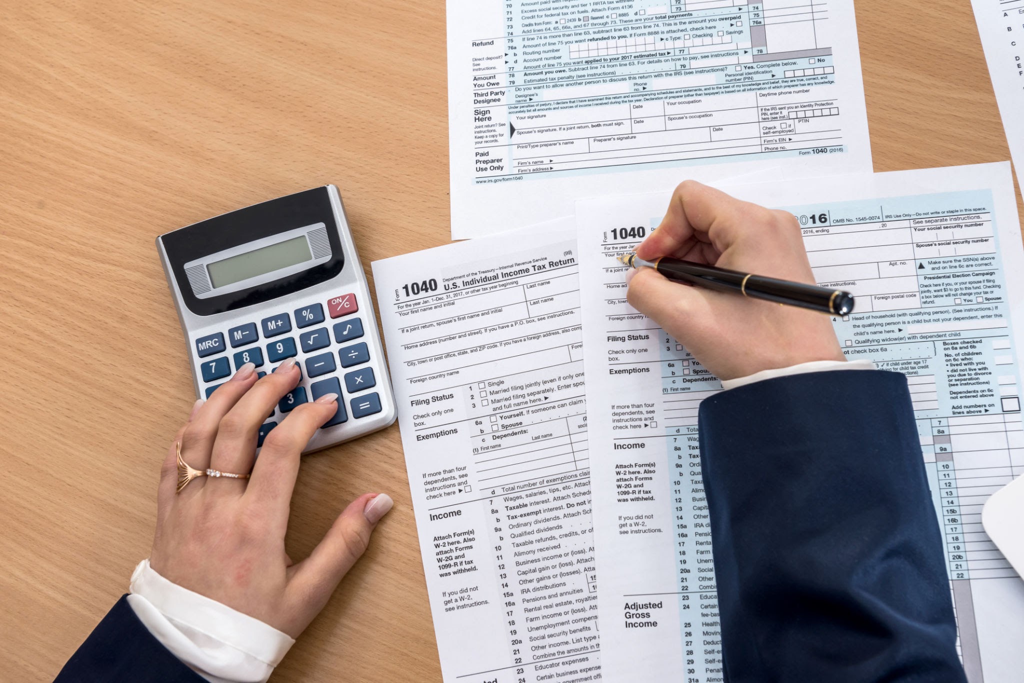 Hands filling income tax return form with calculator and pen on desk