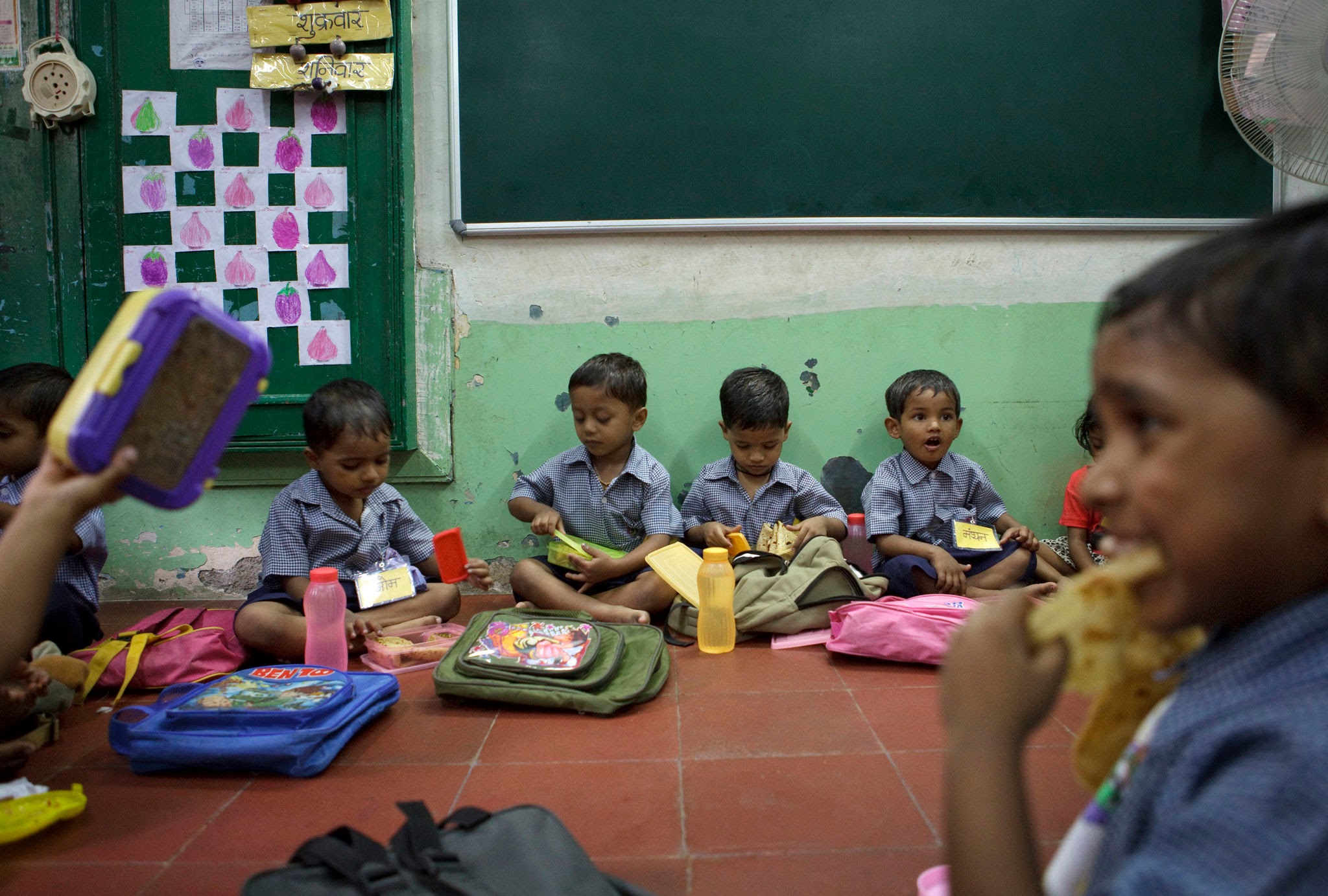 Primary school children sitting together on classroom floor eating mid-day meal