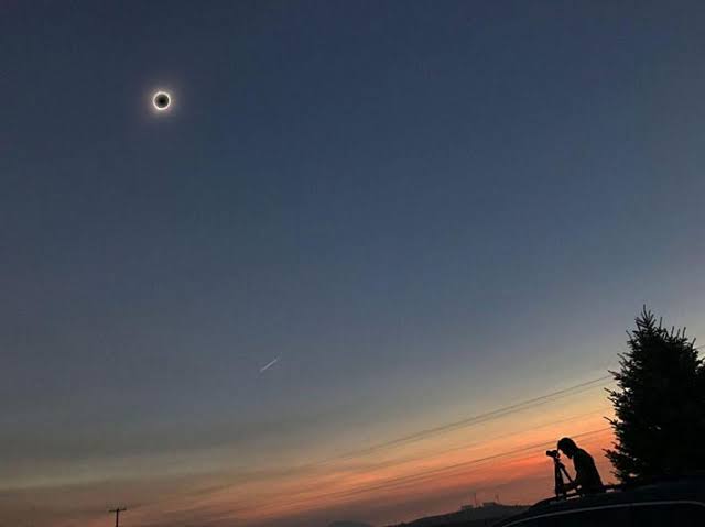 Total solar eclipse with solar corona in twilight sky and photographer silhouetted on vehicle