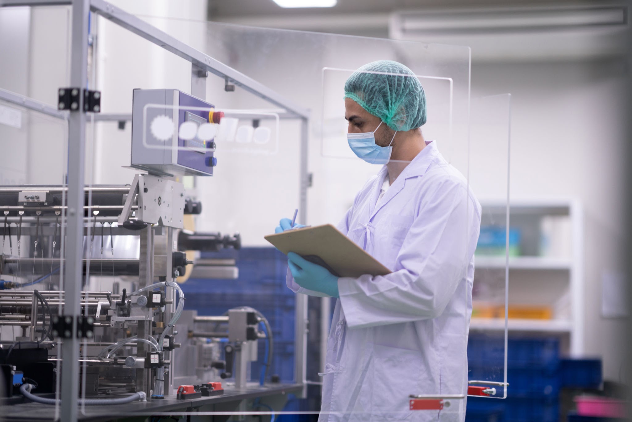 Technician inspecting pharmaceutical packaging machinery in cleanroom